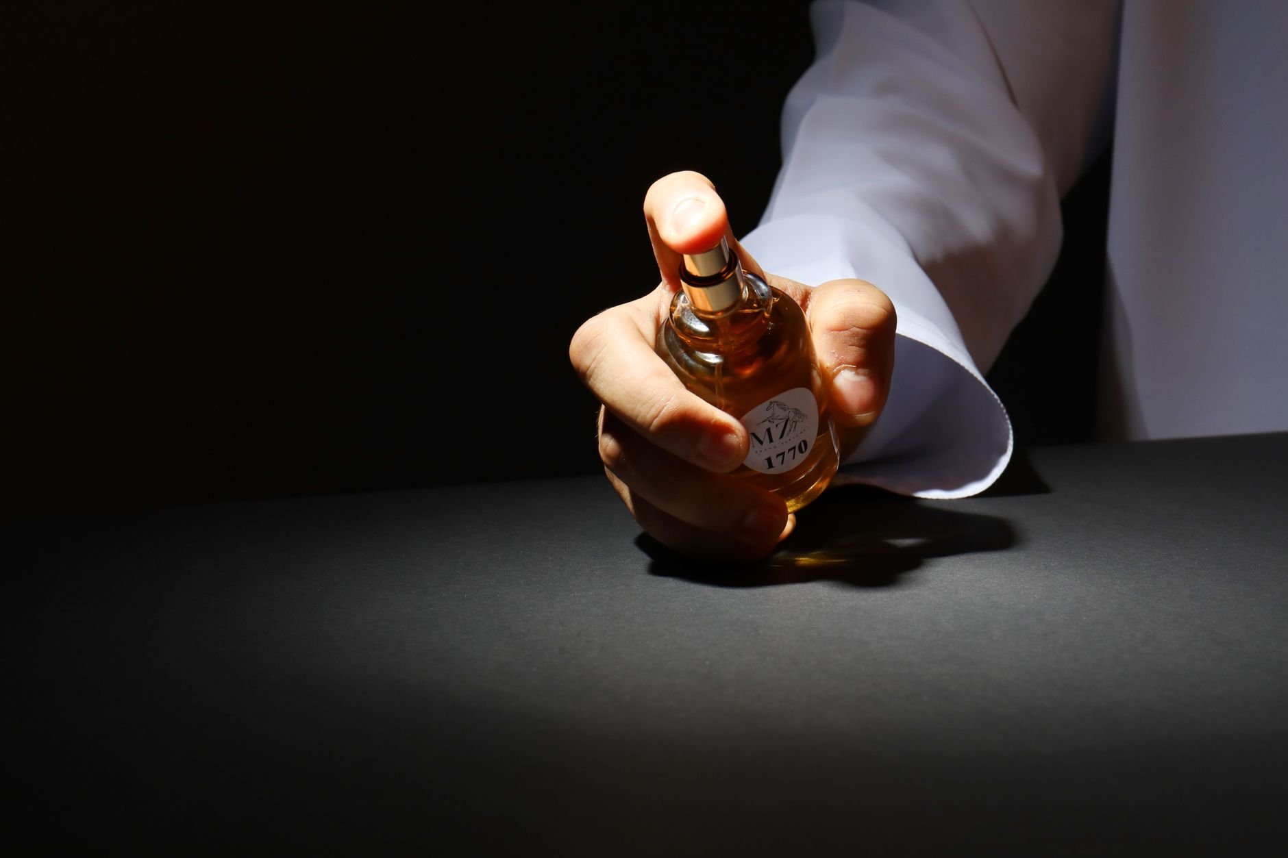 A dramatic close-up of a hand holding a perfume bottle against a dark background, highlighting elegant design.
